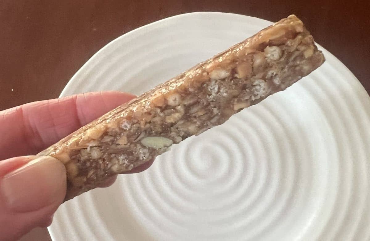 Image of a hand holding one honey cinnamon peanut butter bar close to the camera so you can see the side of the bar. 