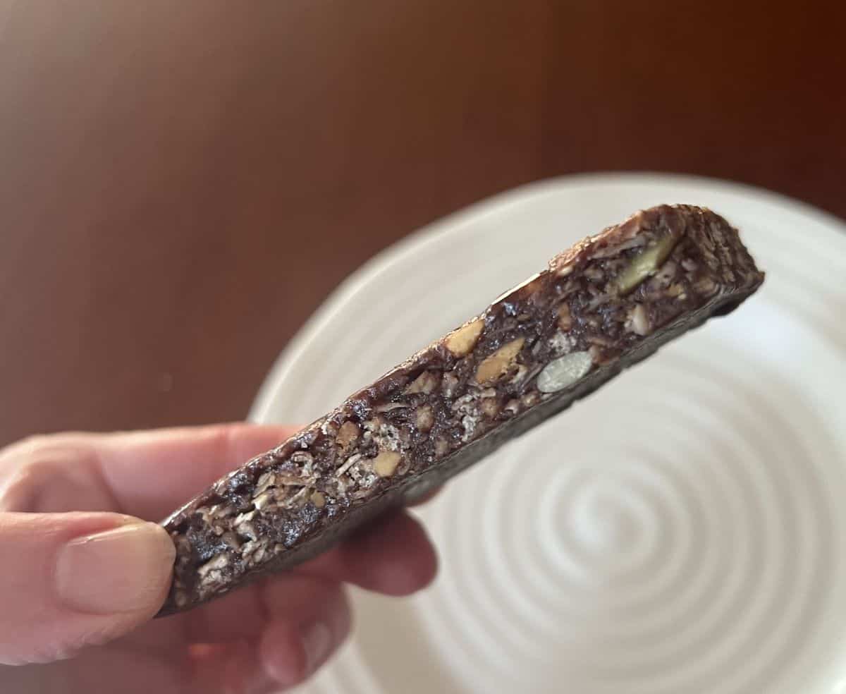 Image of a hand holding one dark chocolate peanut butter bar close to the camera so you can see the side of the bar. 
