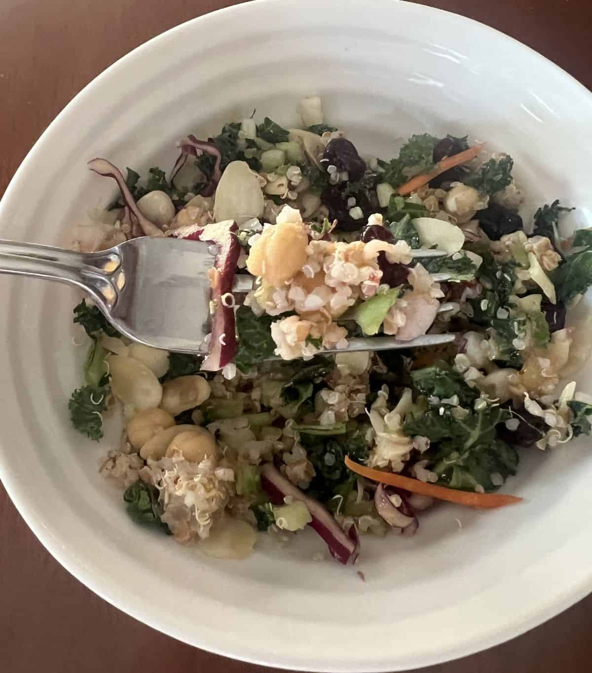 Closeup image of a forkful of salad with chickpeas, grain and kale, hovering over a bowl of the salad.