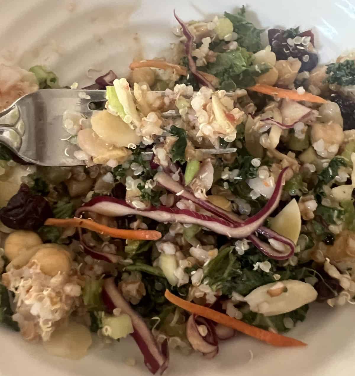 Closeup image of a forkful of salad hovering over a bowl of celery grain salad.