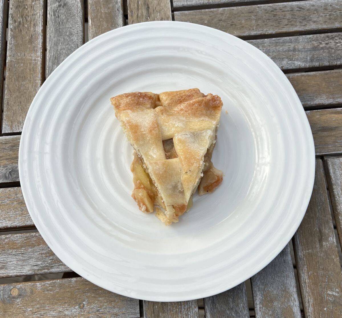 Top down image of one slice of apple pie served on a white plate. 