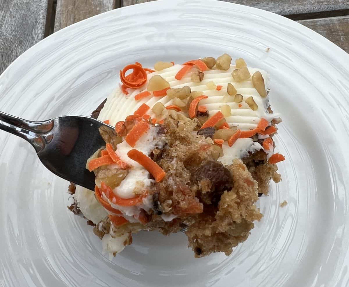 Top down image of a fork with carrot cake on it hovering over a piece of carrot cake.