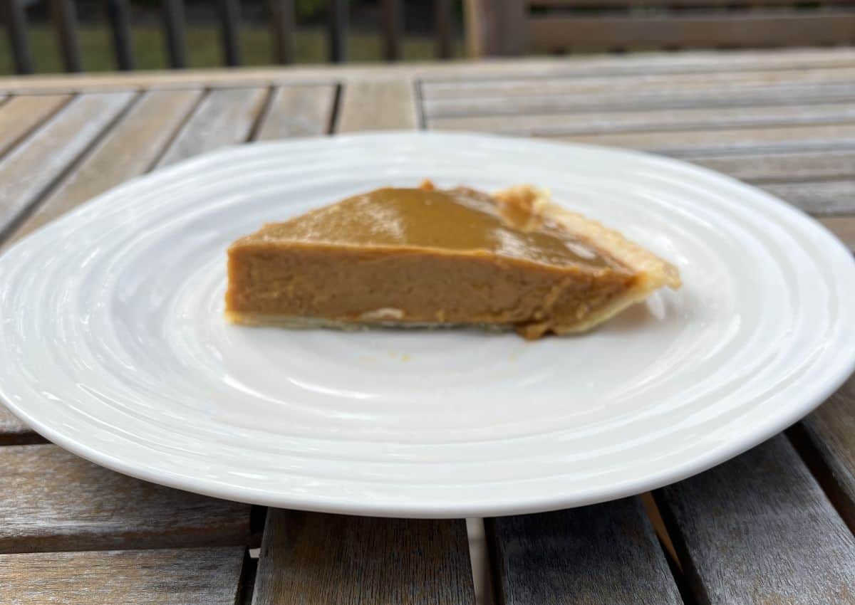 Side view image of a slice of pumpkin pie served on a white plate. 