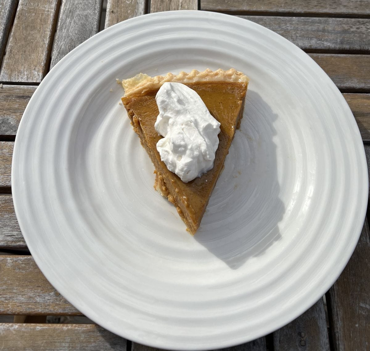 Image of a slice of pumpkin pie served on a white plate with whipped cream on it.