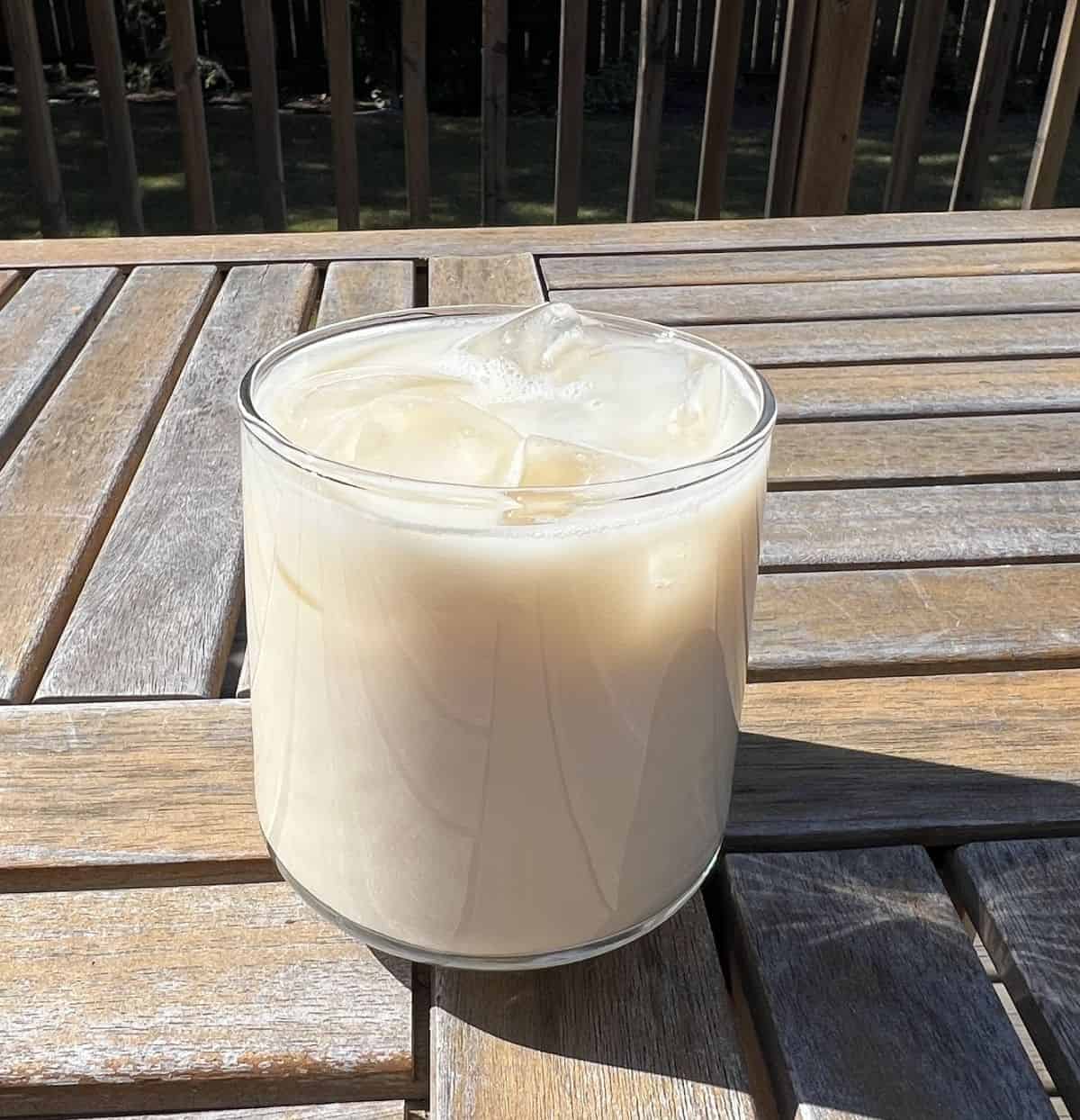 Side view image of one Premier Protein Pumpkin Spice protein shake poured and served into a clear glass with ice.
