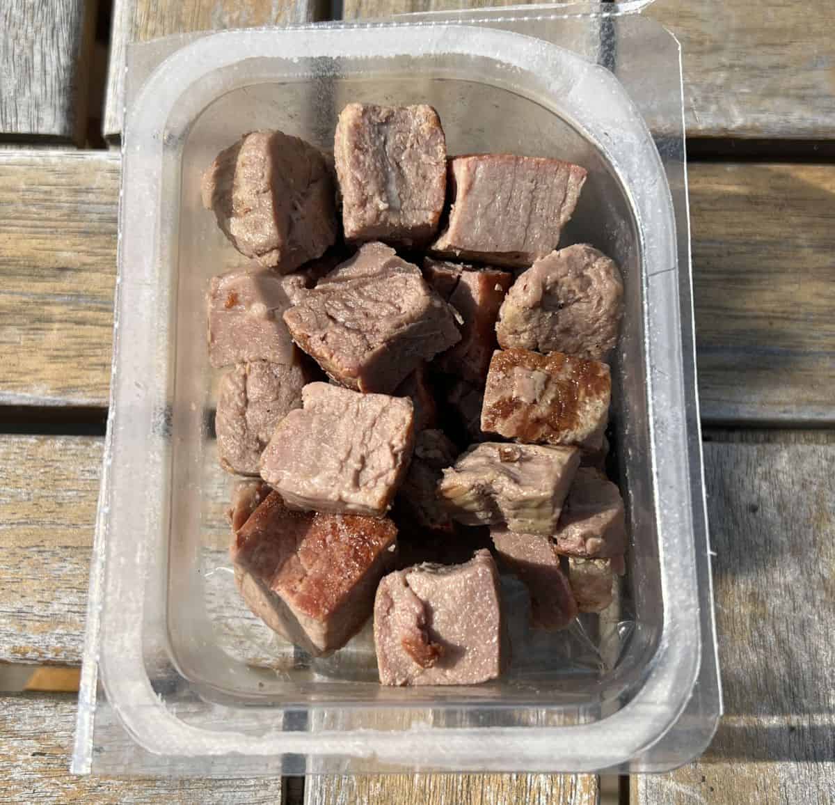 Top down closeup image of an open package of steak bites sitting on a table outside.
