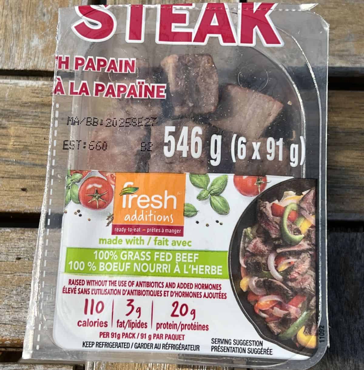 Image of one 91 gram pack of steak bites sitting on a table unopened.