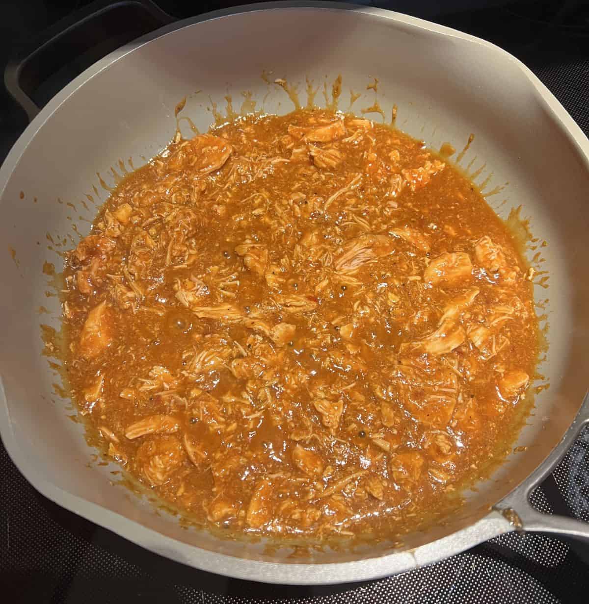 Top down image of the chicken tinga being cooked in a pan on the oven.