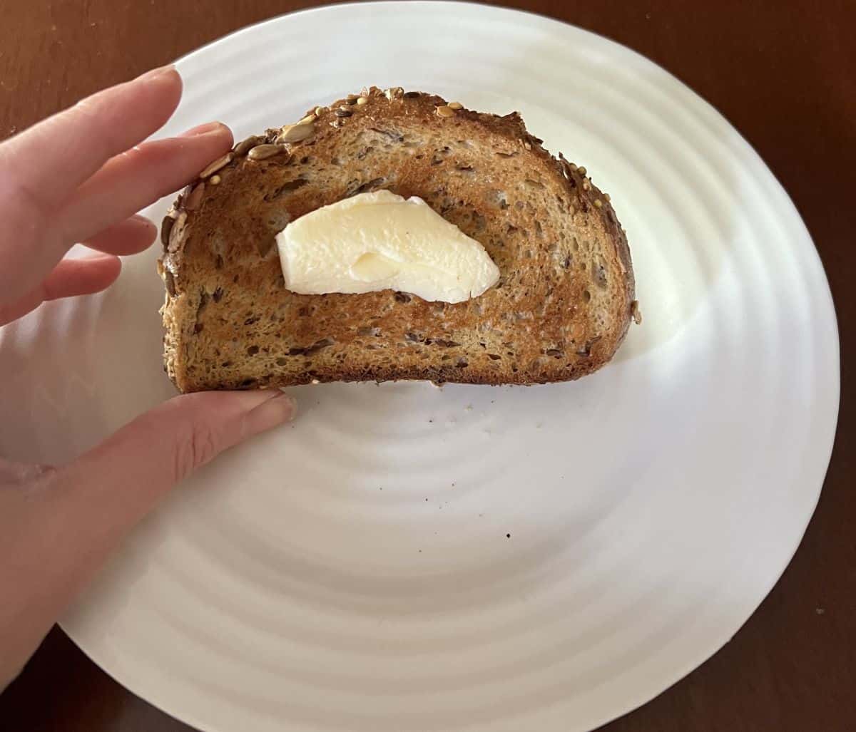 Image of a hand holding one slice of bread toasted with butter on it.