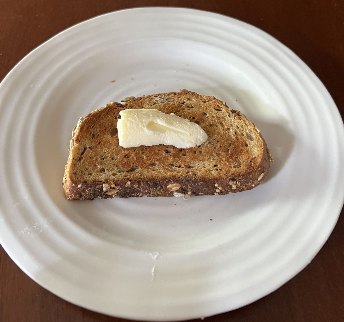 Image of a slice of bread toasted with butter served on a white plate.