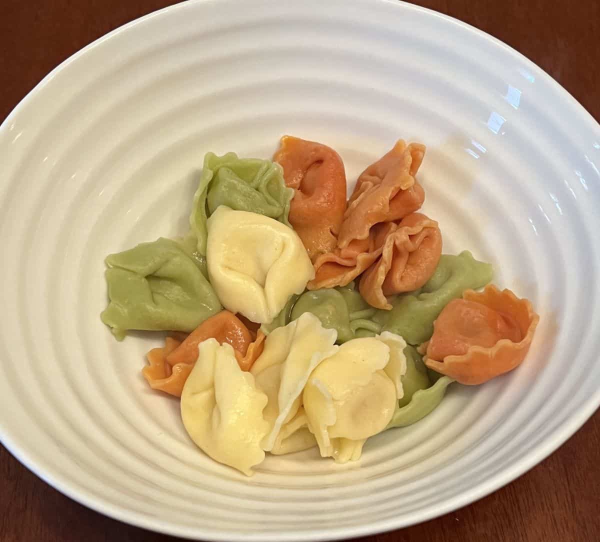 Top down image of a bowl of plain cooked rainbow tortellini. 