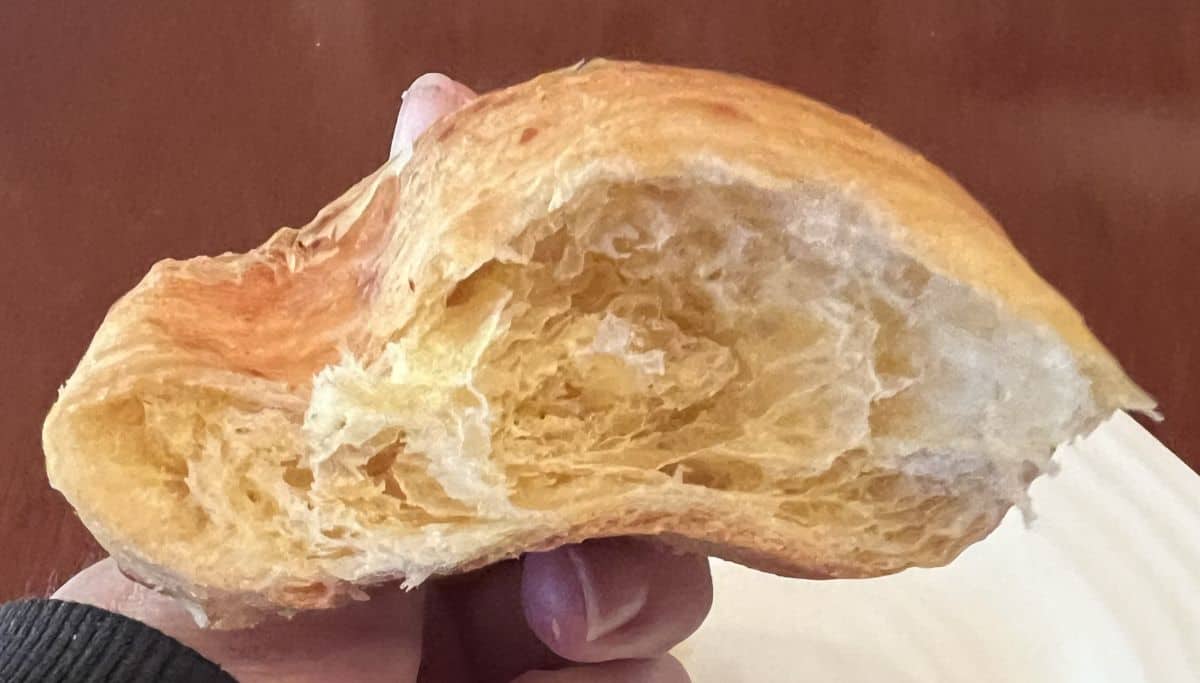Image of a hand holding one croissant cut in half so you can see the center. 