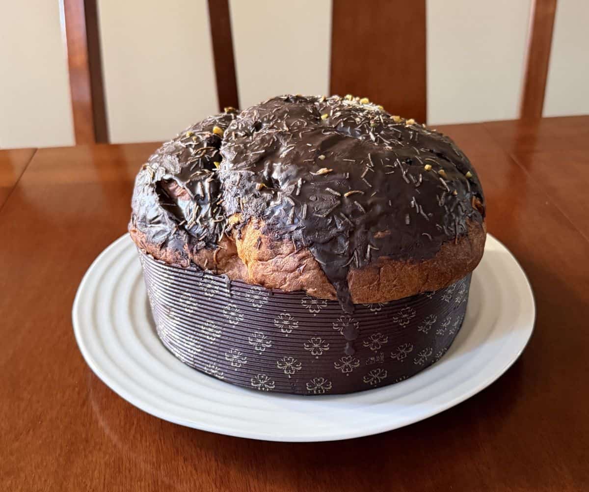 Image of the entire panettone served on a white plate in the wrapper. 