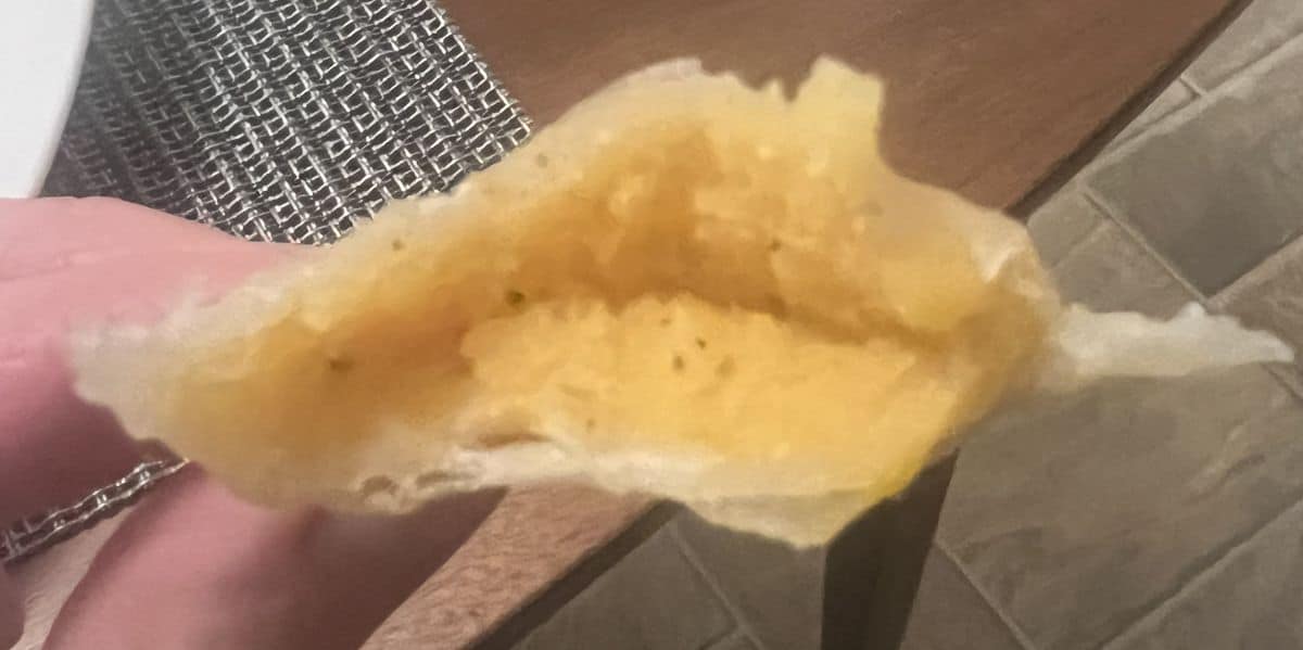 Image of a hand holding one perogie cut in half so you can see the filling. 