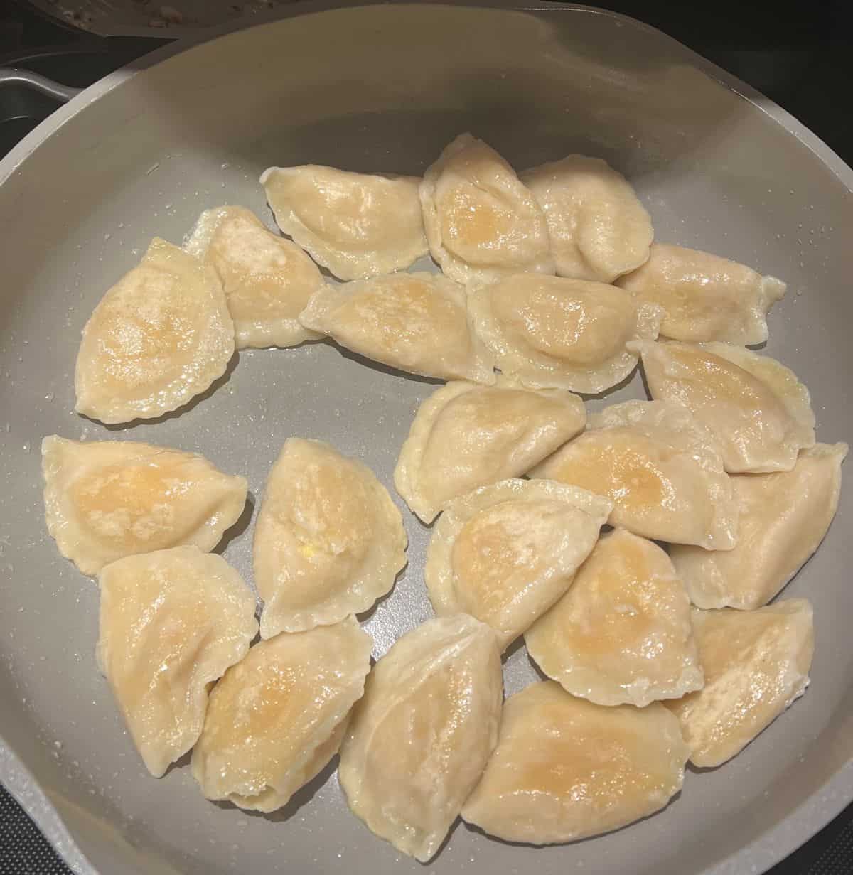 Image of the perogies being cooked in a pan after being boiled.