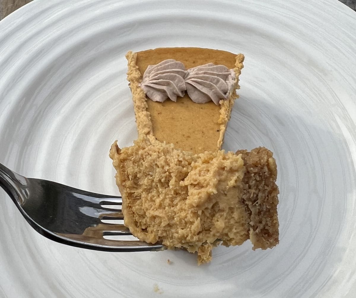 Image of a bite of pie on a for hovering over a plate with a slice of cheesecake on it.