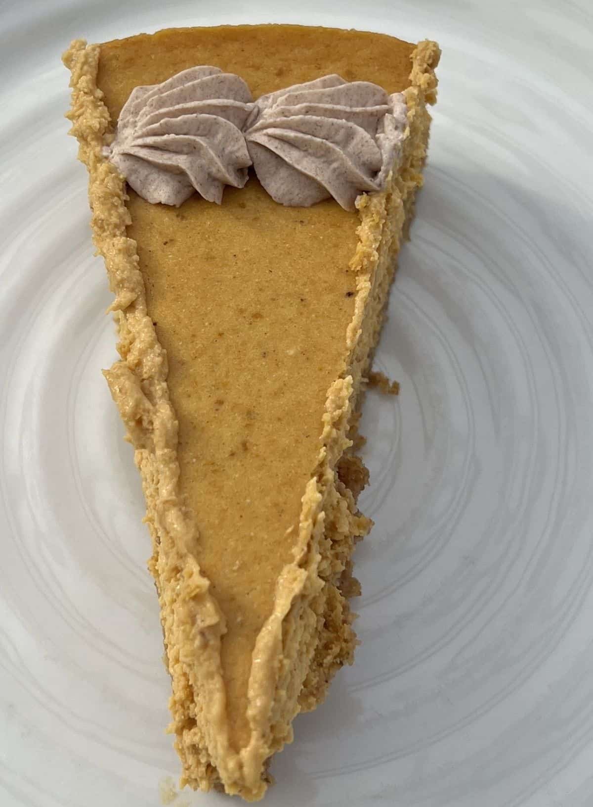 Closeup top down image of one slice of cheesecake with cinnamon frosting on top served on a white plate.