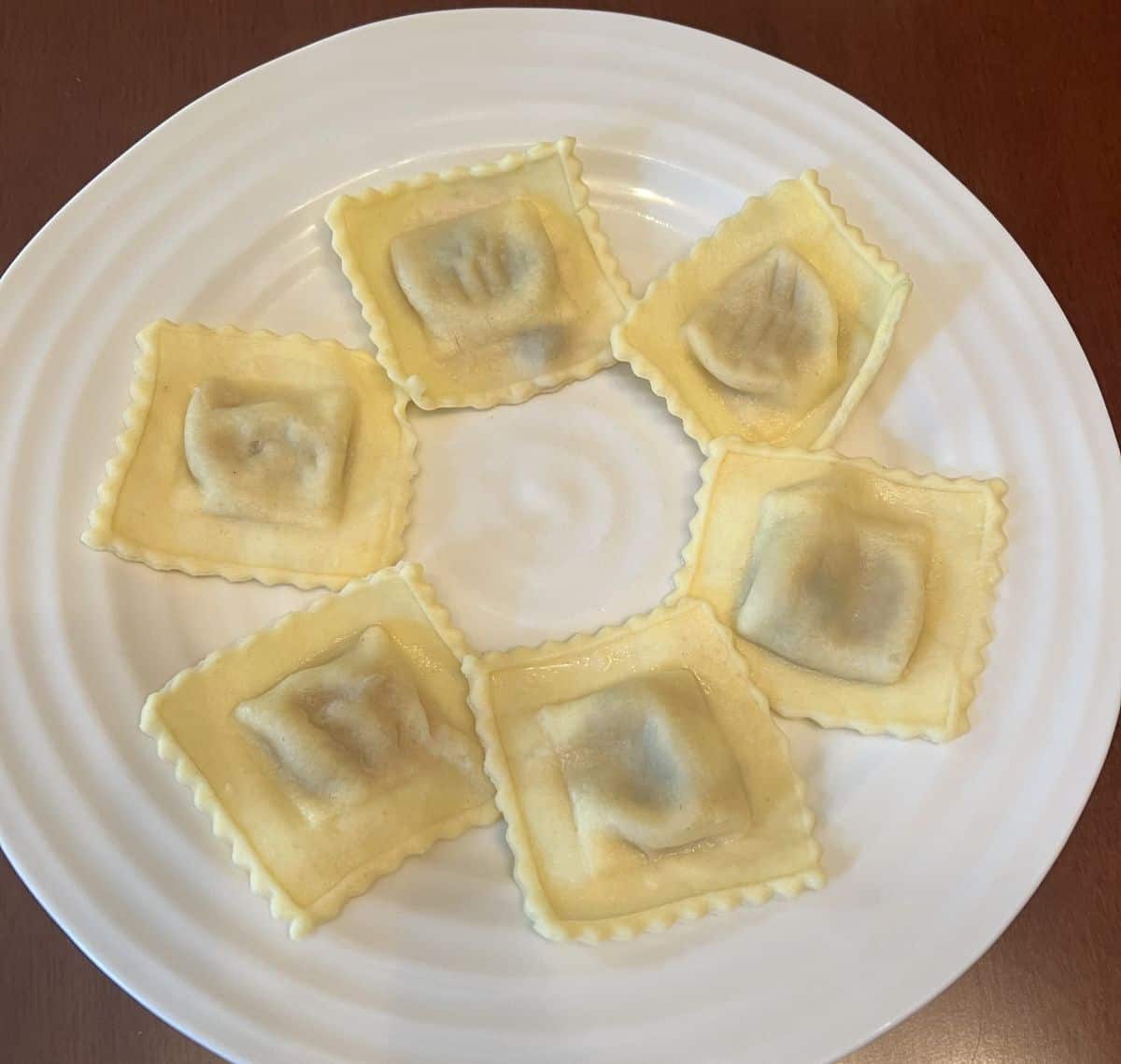 Image of six ravioli served on a white plate. 