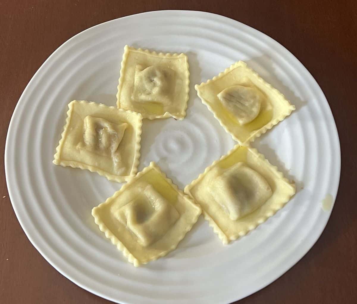 Image of five ravioli pieces served on a white plate drizzled with olive oil. 