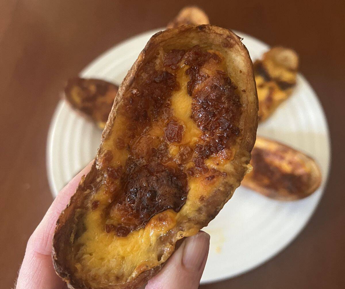 Image of a hand holding one potato skin close to the camera hovering over a plate of potato skins.