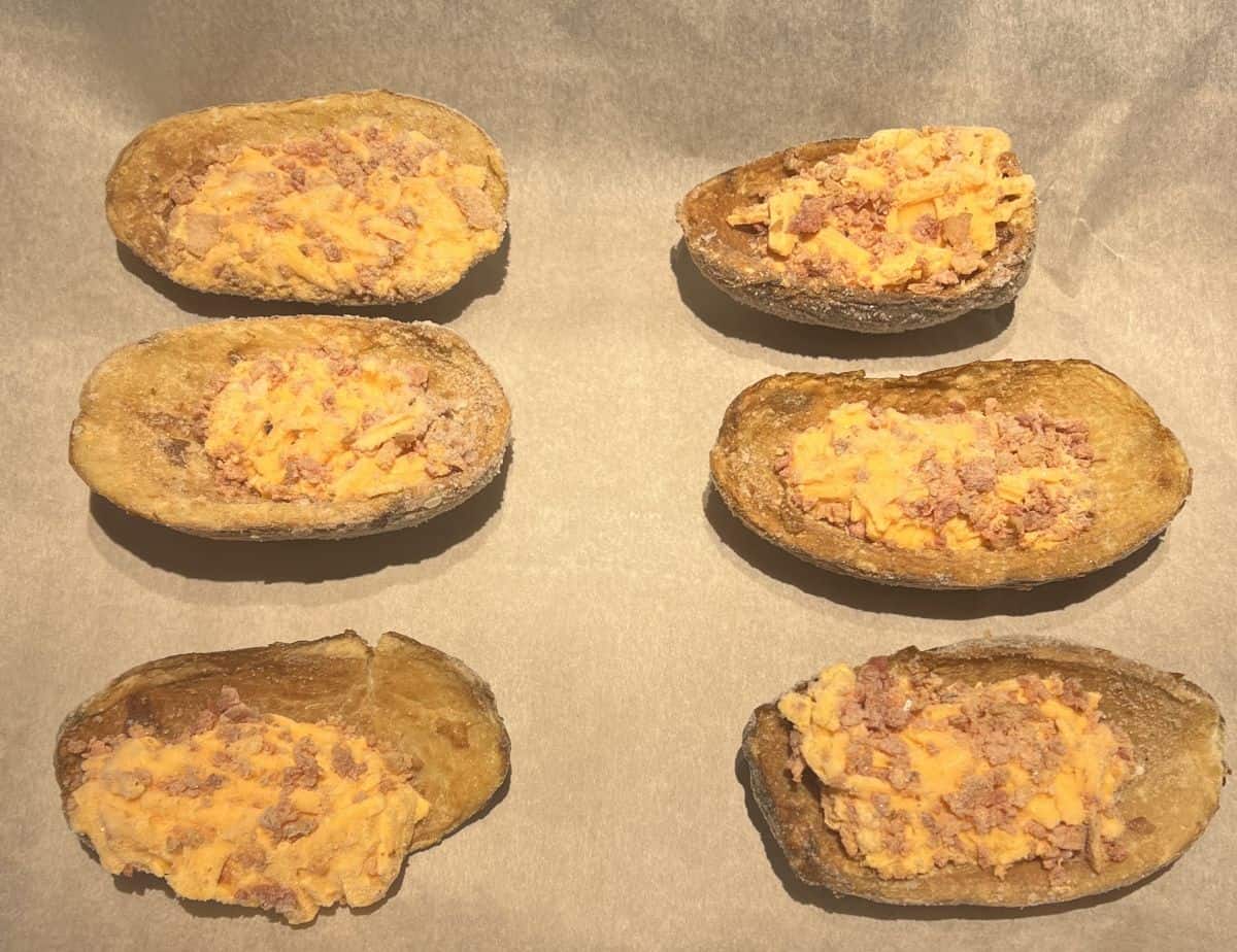 Image of six frozen potato skins on a parchment paper lined cookie tray before going into the oven.