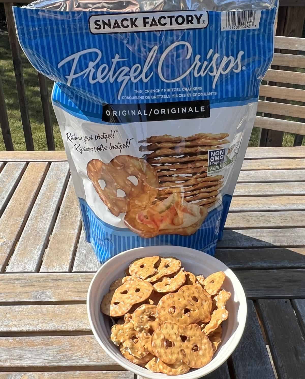Image of a bag of pretzel crisps sitting on a table outside with a bowl of pretzel crisps sitting in front of it.