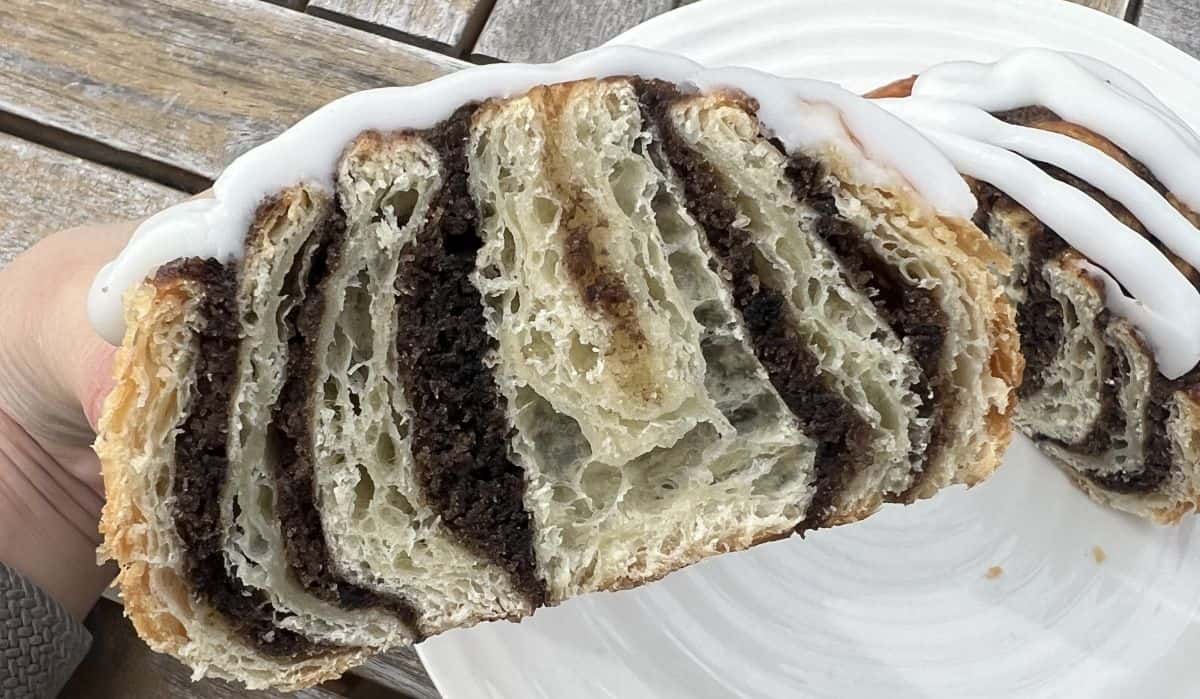 Closeup image of a hand holding one cookies & cream swirl that's been cut in half so you can see the inside.