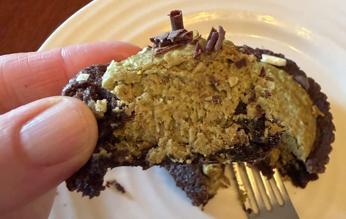 Image of a hand holding one piece of Dubai brownie close to the camera so you can see the pistachio cream filling.