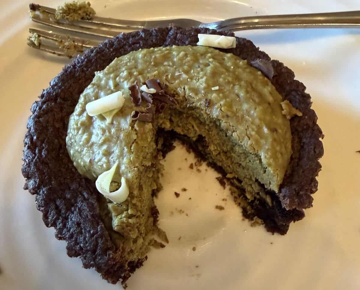 Closeup image of one brownie served on a white plate with a section cut out so you can see the center of the brownie.