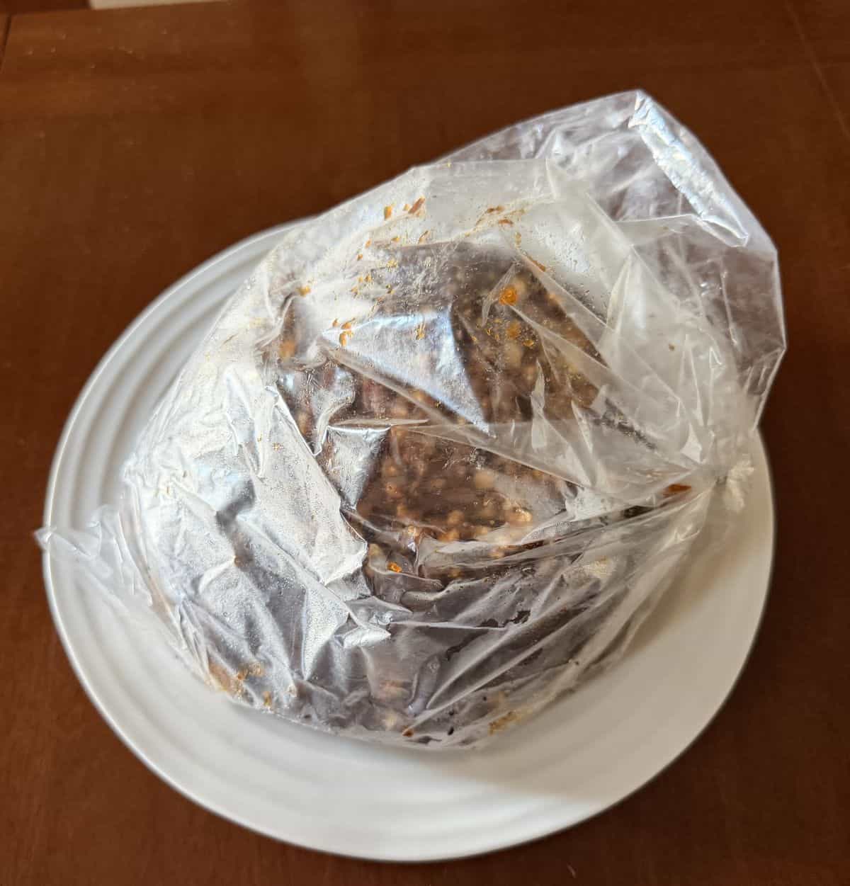 Image of the cake wrapped in a plastic bag and sitting on a plate on a table.
