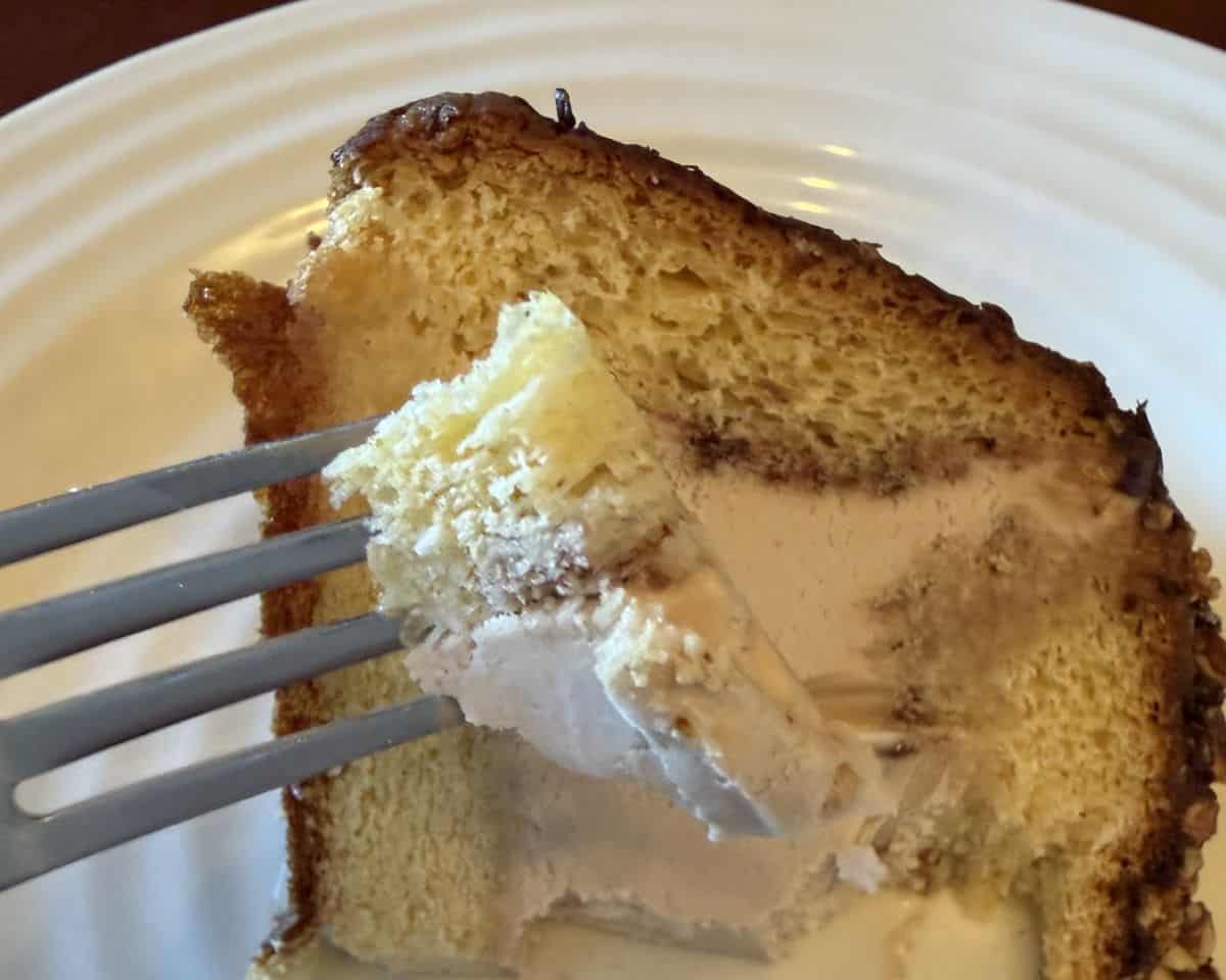 Closeup image of a fork with cake and ice cream on it hovering over a piece of cake.