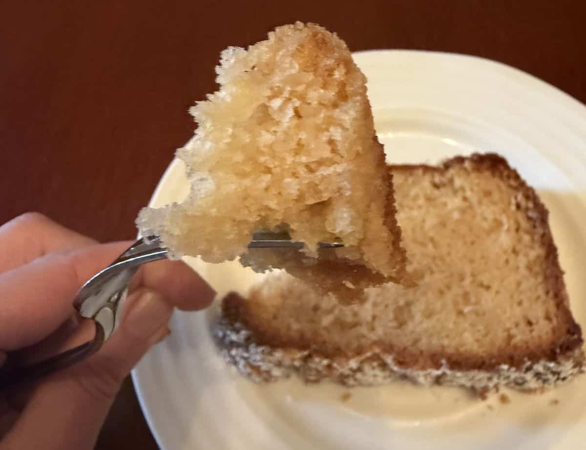 Image of a fork with one bite of chai spiced loaf cake on it hovering over a plate. 