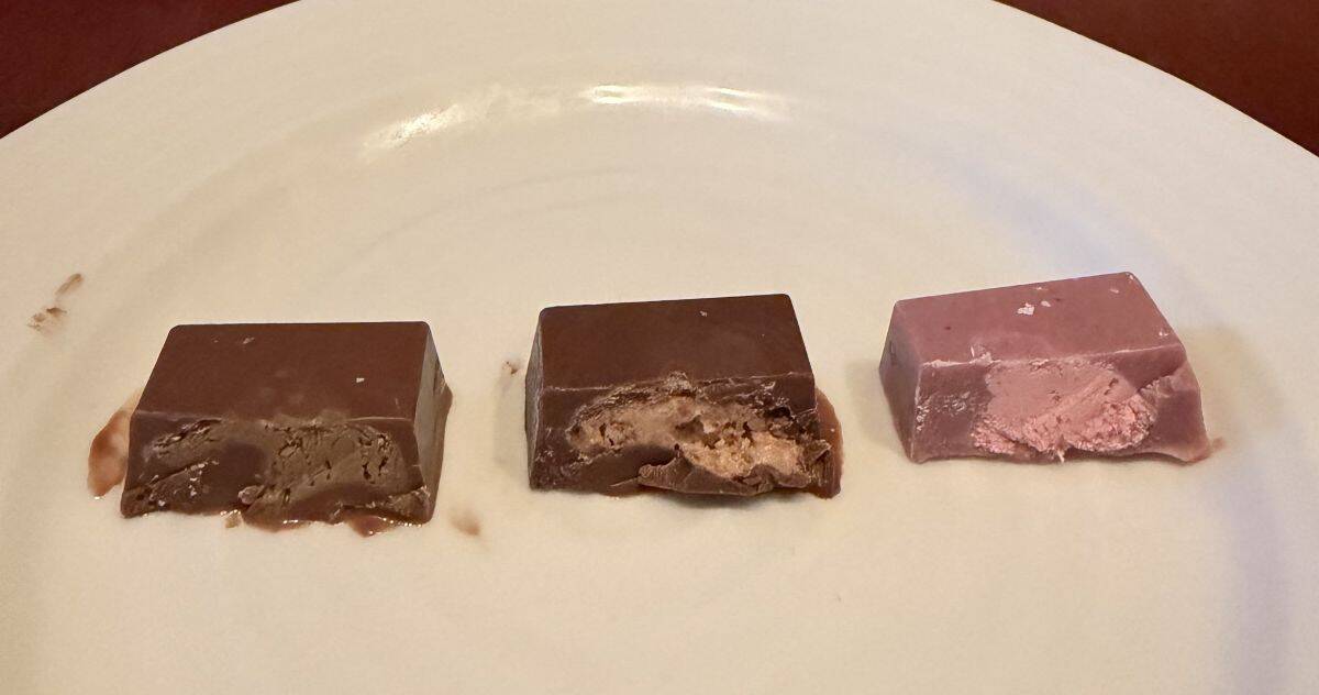 Image of three chocolates served on a white plate and cut in half so you can see the center. There is pistachio, hazelnut and strawberry.