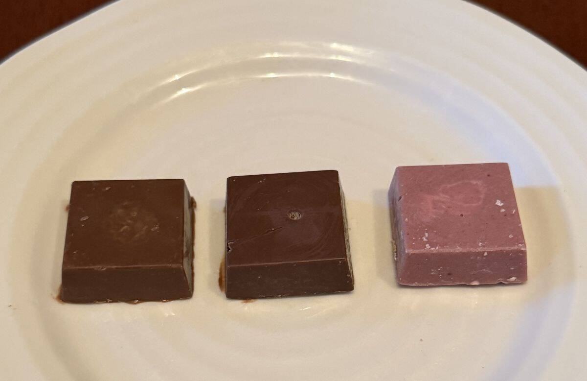 Image of three chocolates served on a white plate, hazelnut, pistachio and strawberry.