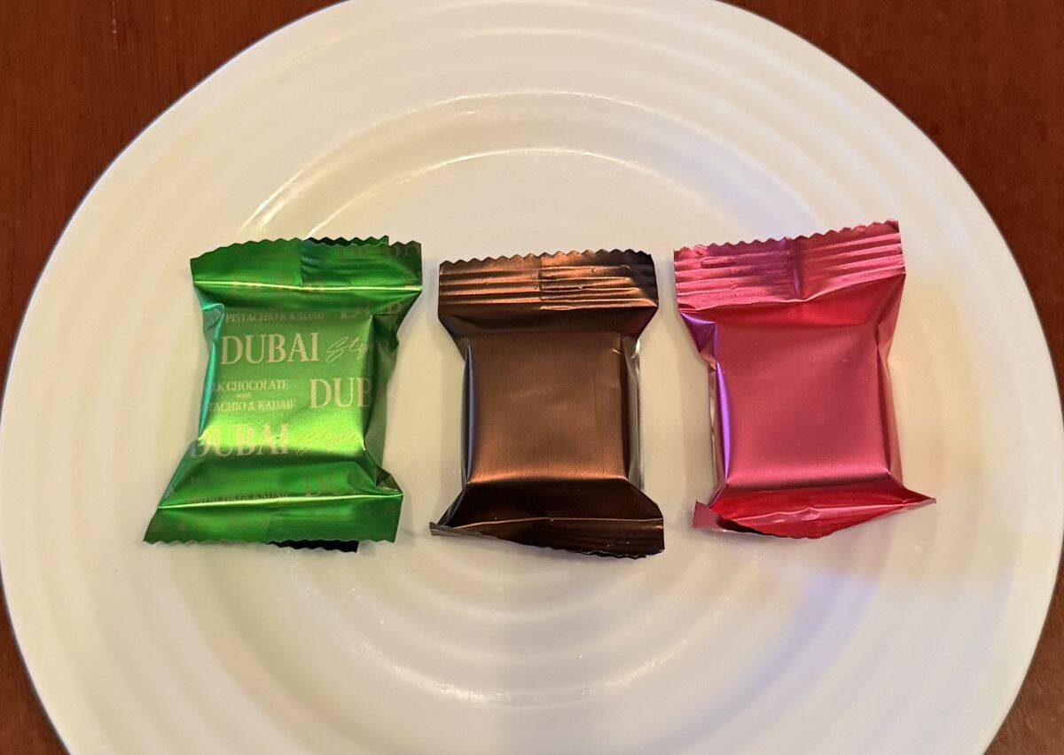 Image of three individually wrapped chocolates on a plate, there is a green one, a brown one and a pink one.