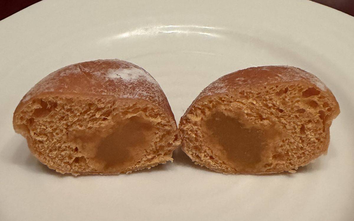 Image of one passionfruit mini filled donut cut in half so you can see the filling inside. 