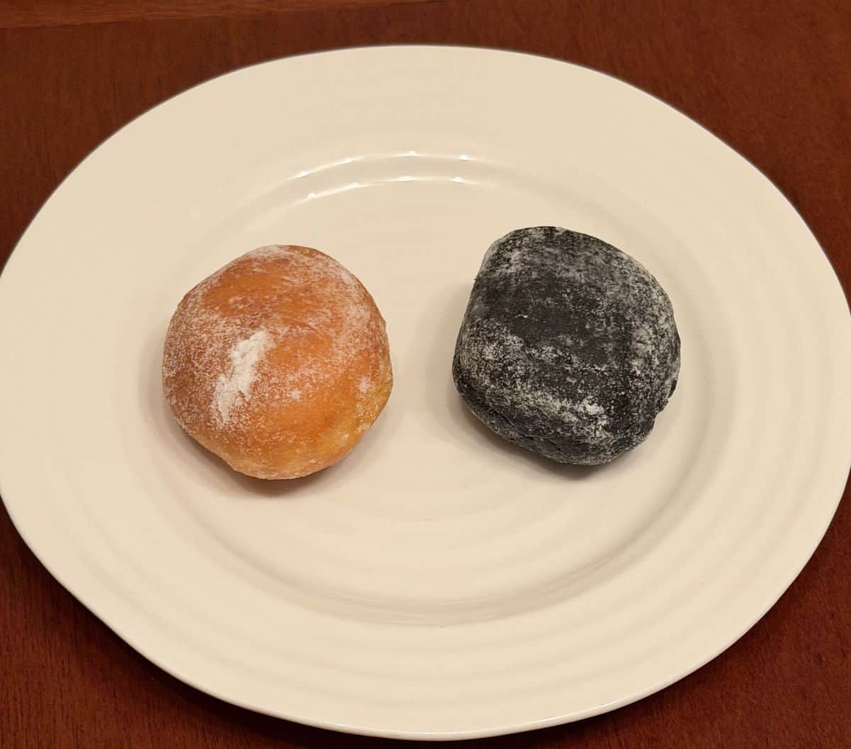 Image of two mini donuts one black, one orange served on a white plate. 