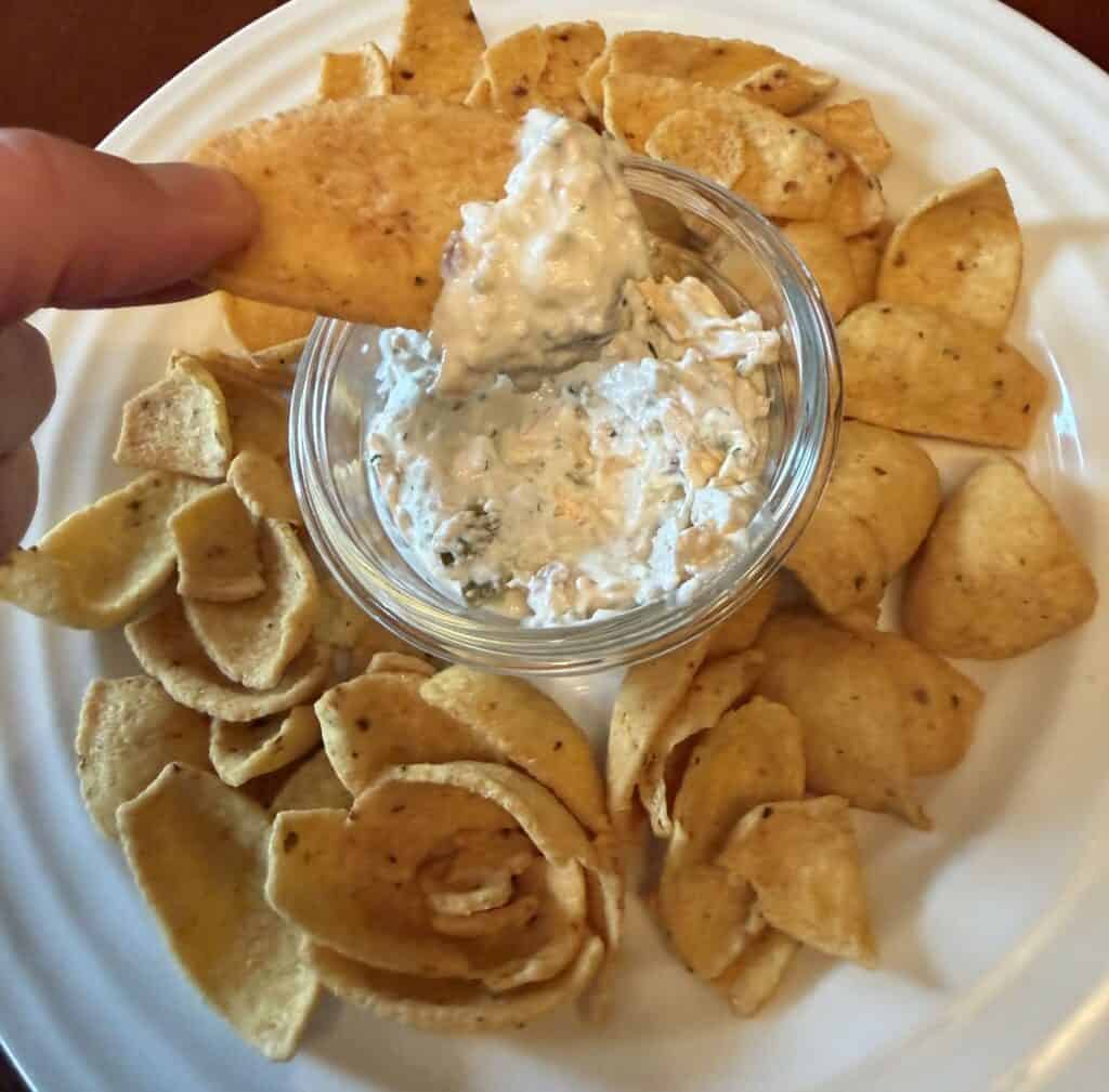 Image of a hand holding a chip that's been dipped hovering over a plate with chips and dip on it.