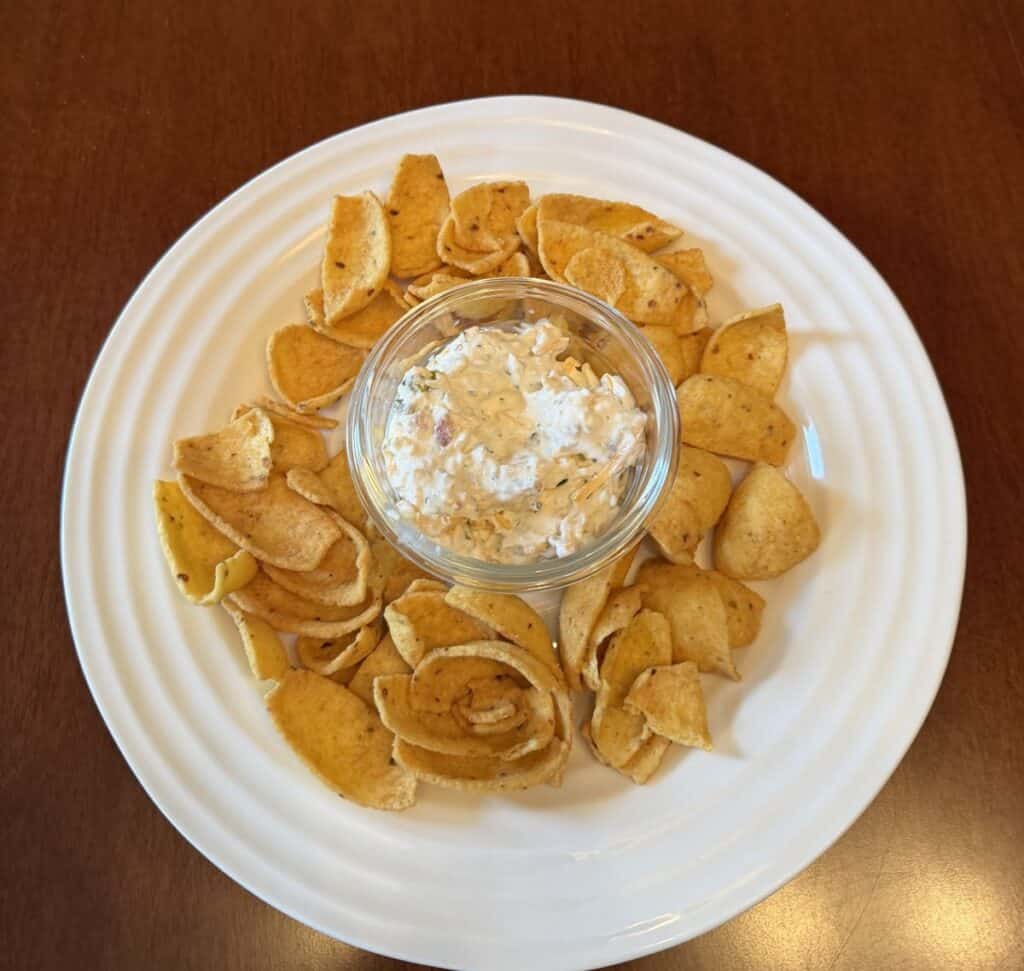 Image of a bowl of dip in the center of a plate with corn chips surrounding it.