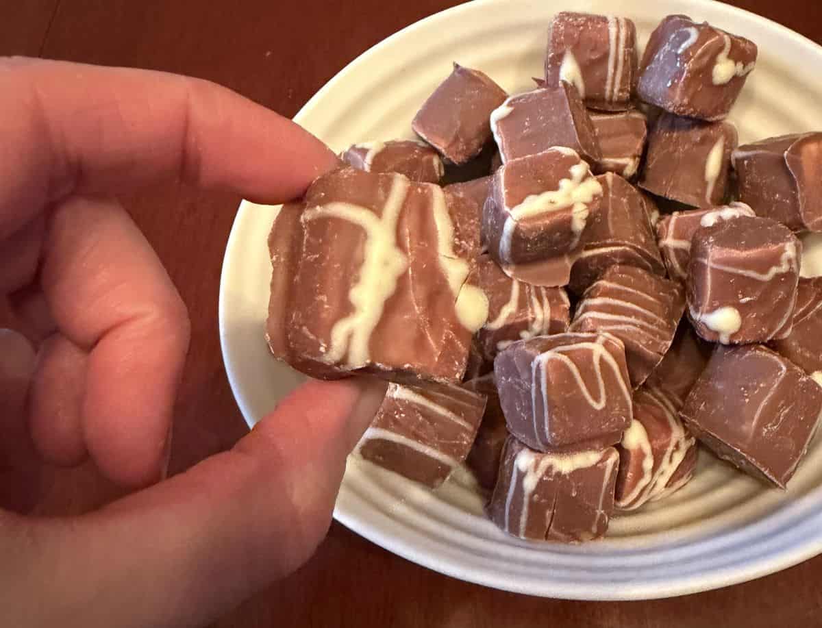 Image of a hand holding one mallow close to the camera hovering over a bowl of Mallows.