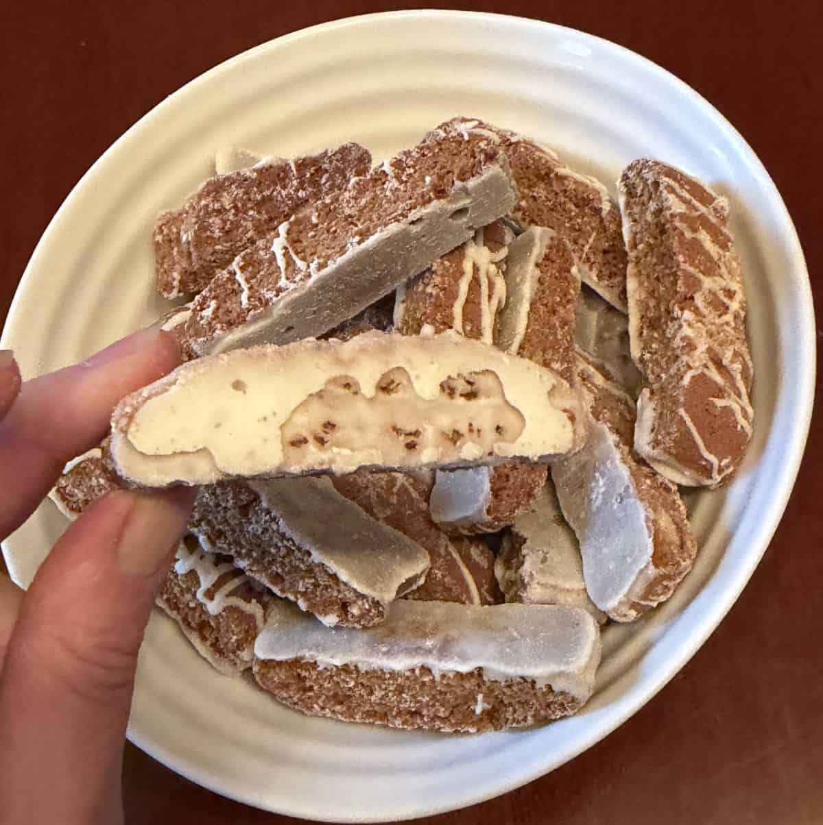 Image of a hand holding one biscotti bite with the glazed side facing the camera.
