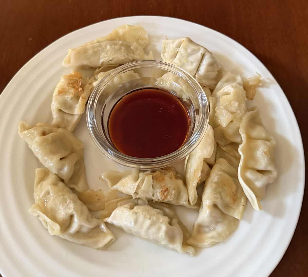 Top down image of cooked potstickers served on a white plate with dipping sauce in the middle. 