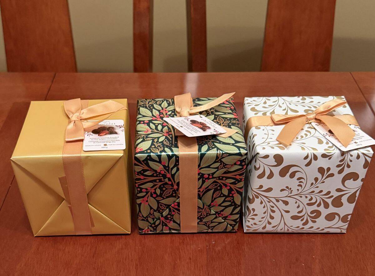 Image of the three boxes of wrapped chocolates with bows on them sitting on a table unopened.