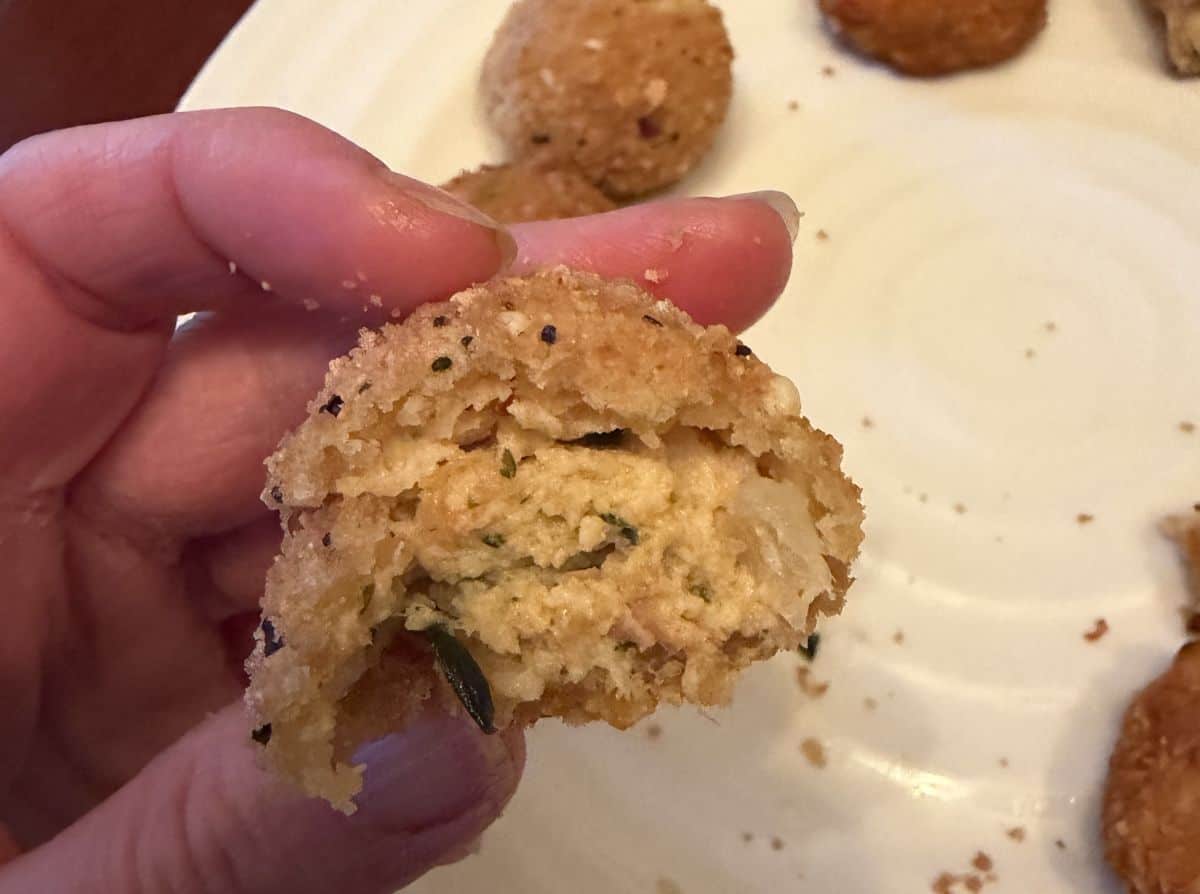 Image of a hand holding one smoked salmon bite close to the camera.