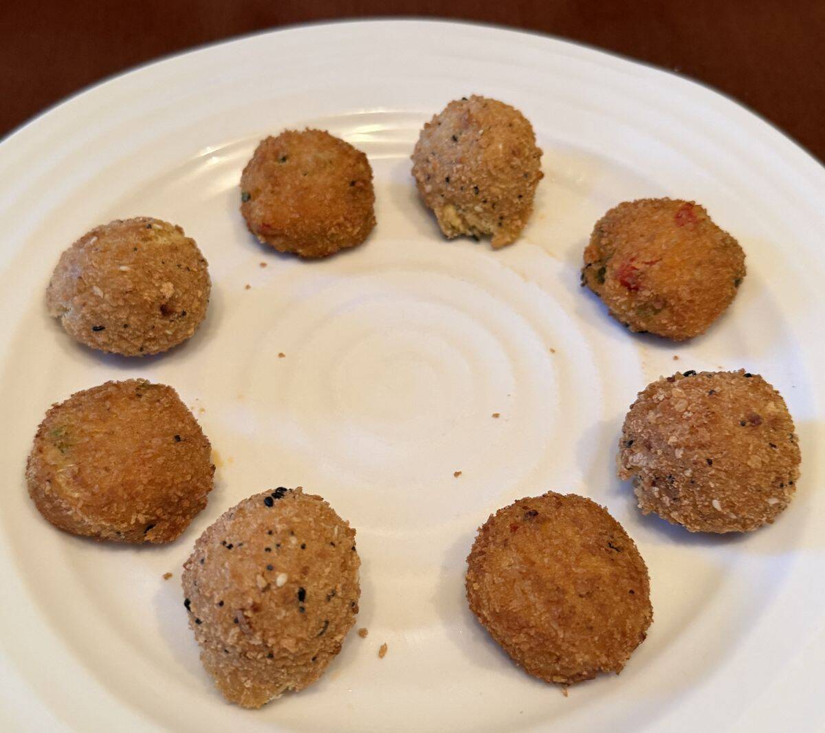 Image of a white plate with eight cooked salmon and crab cake bites served on it.
