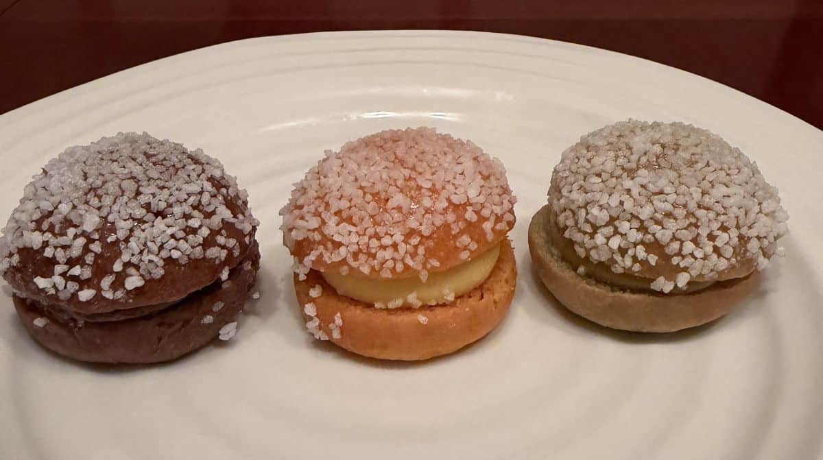 Closeup top down image of three mini brioche filled with pastry cream served on a white plate.