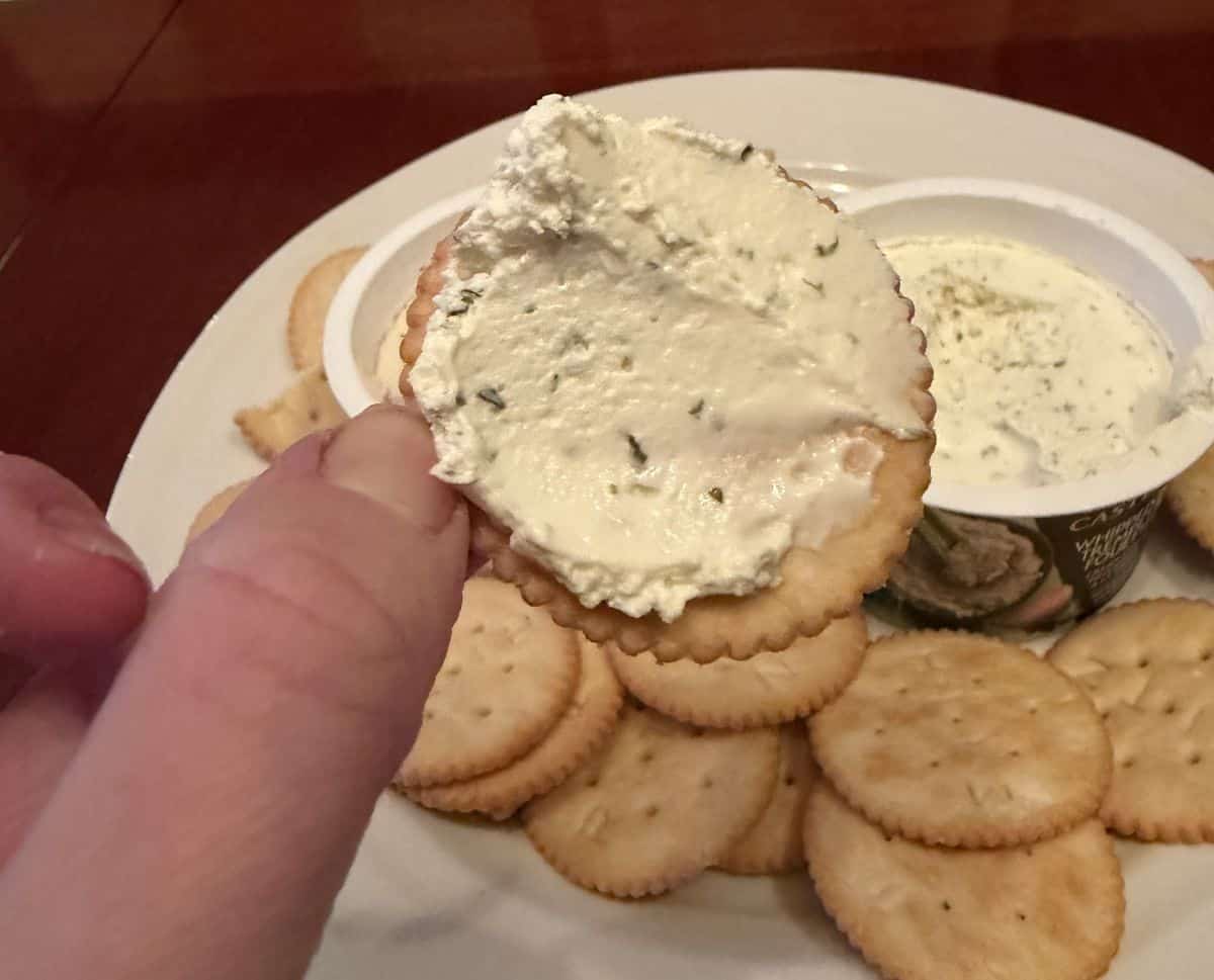 Image of a hand holding a cracker close to the camera with herb & garlic dipped on it.