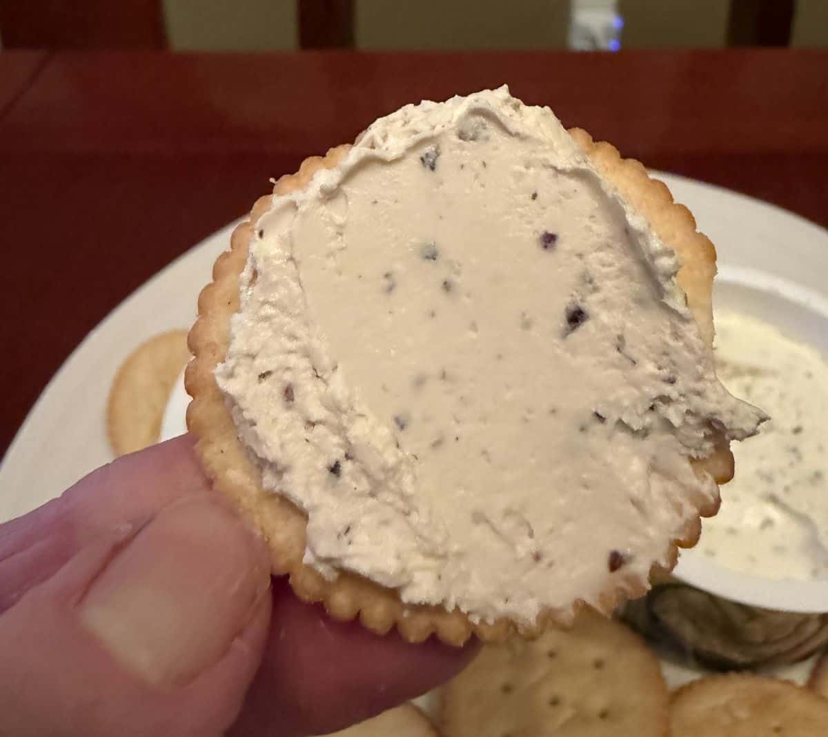 Image of a hand holding a cracker with cracked pepper dip on it close to the camera.