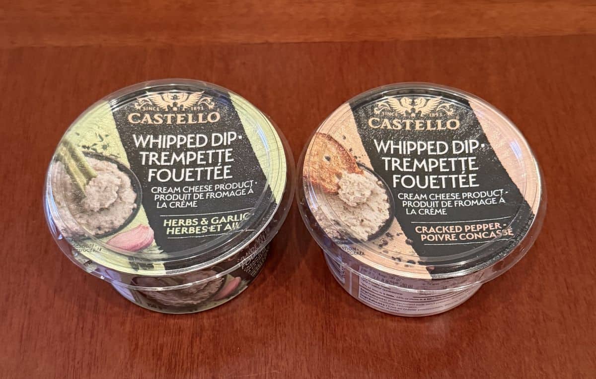 Image of a herb & garlic dip beside a cracked pepper dip unopened on a table.