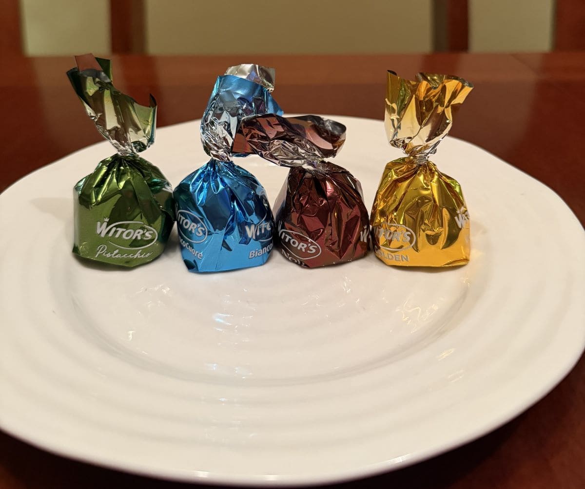 Image of four individually wrapped truffles served on a white plate. The wrappers are four different colors.